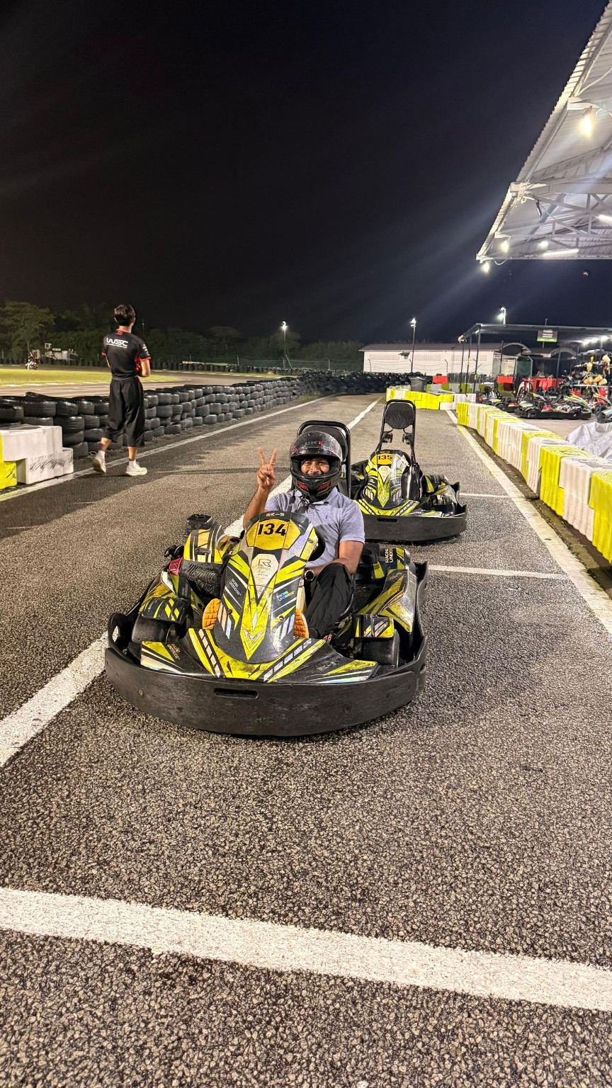 Thana wearing a helmet and sitting in a go-kart at a track at night