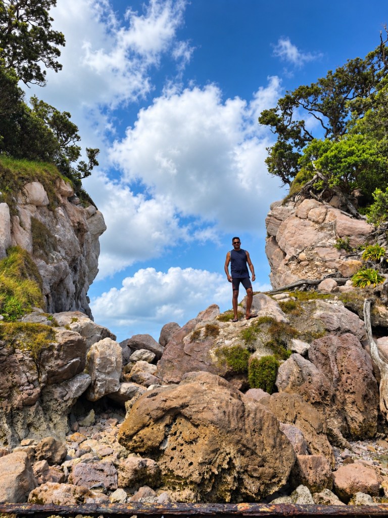 Thana standing among large rocks under a bright sky during a trip