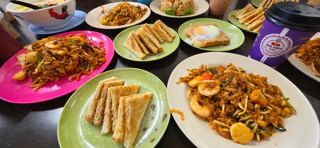 A table filled with noodles, toasted sandwiches, eggs and coffee