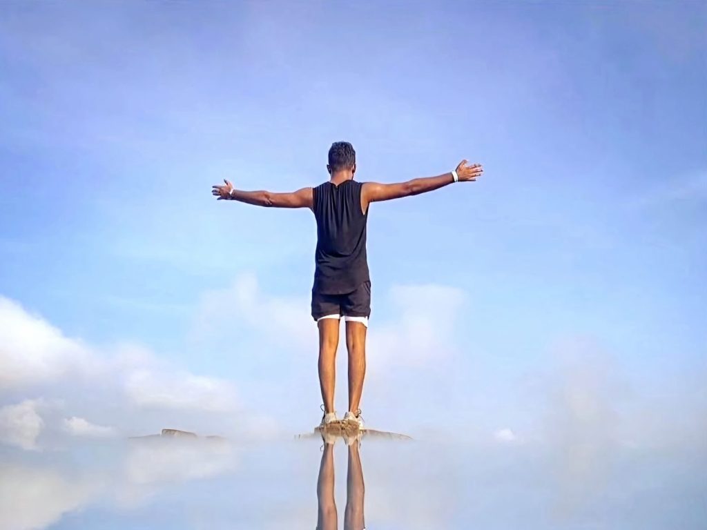 Thana with arms outstretched above a sea of clouds.