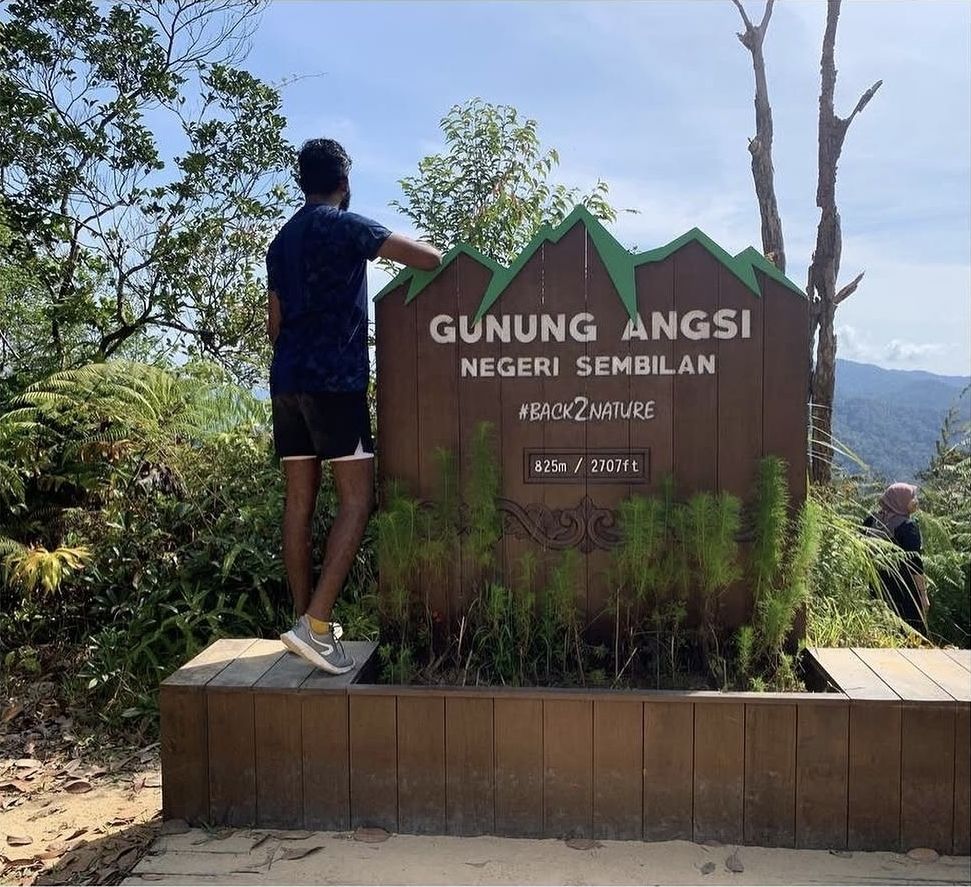 A hiker beside the Gunung Angsi summit sign in Negeri Sembilan