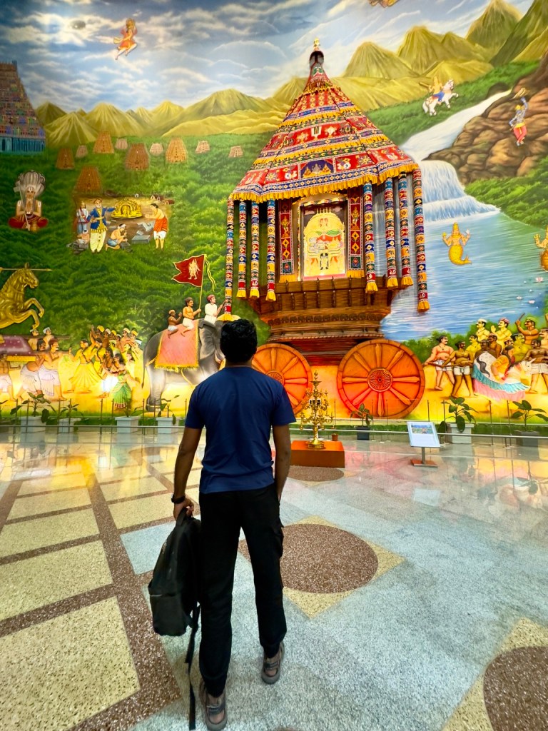 Thana standing before a colourful temple mural