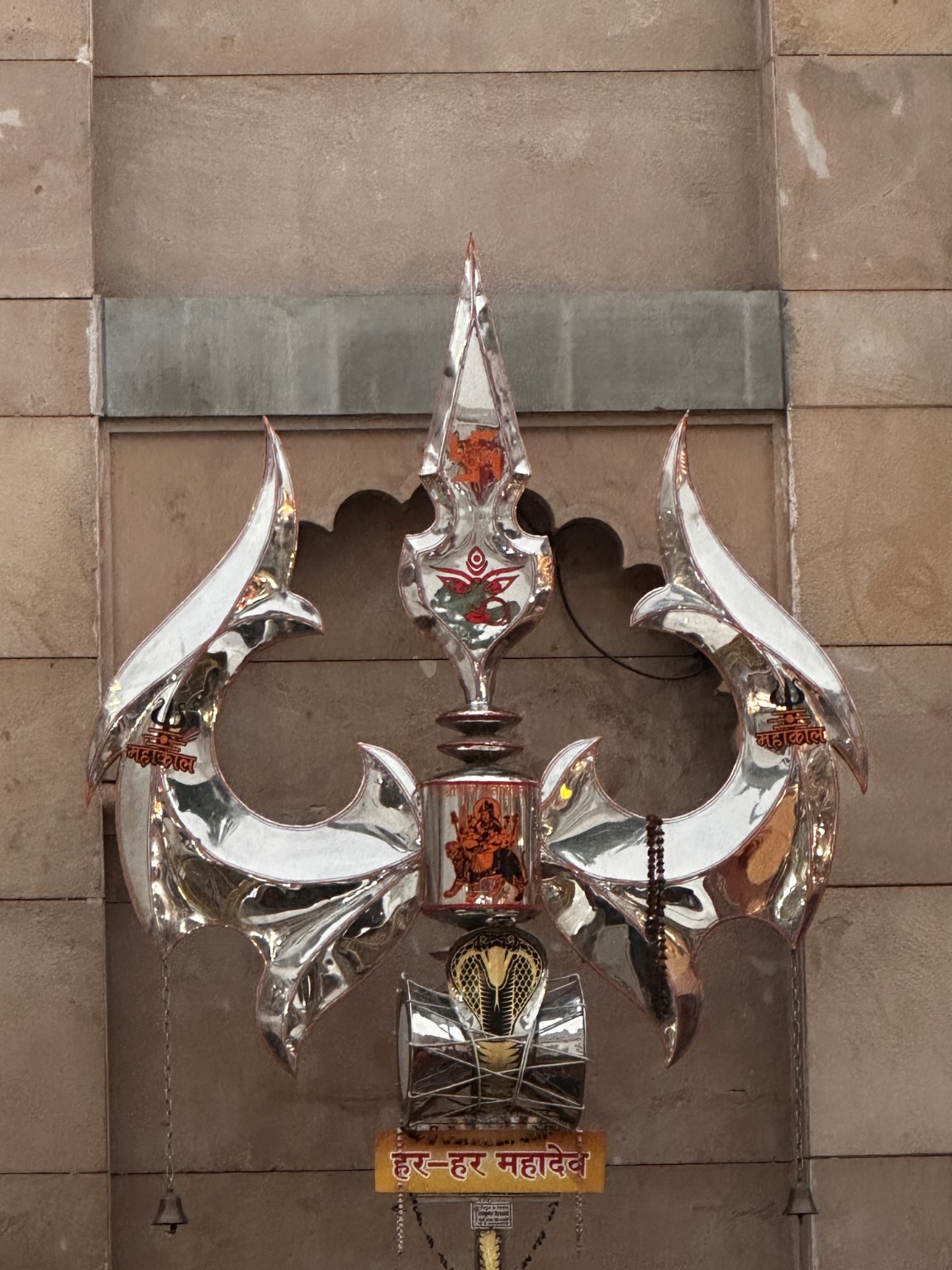 A silver trishul with a damaru and Har Har Mahadev inscription.