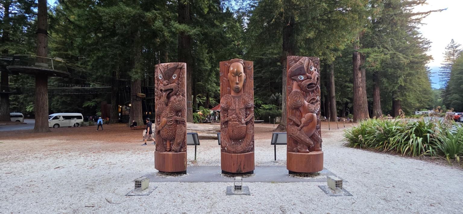 Three carved wooden figures among trees in New Zealand