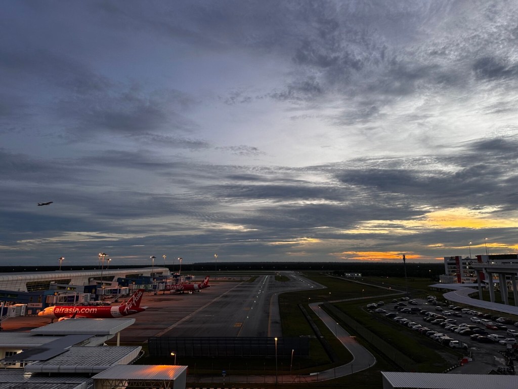Planes and airport grounds beneath a cloudy sky with warm light along the horizon