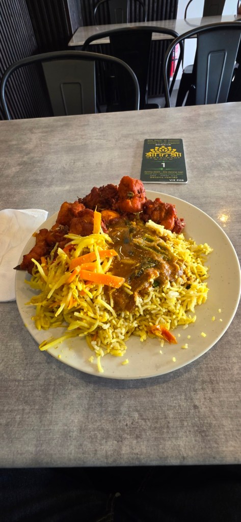 A plate of briyani with curry, vegetables and fried pieces.