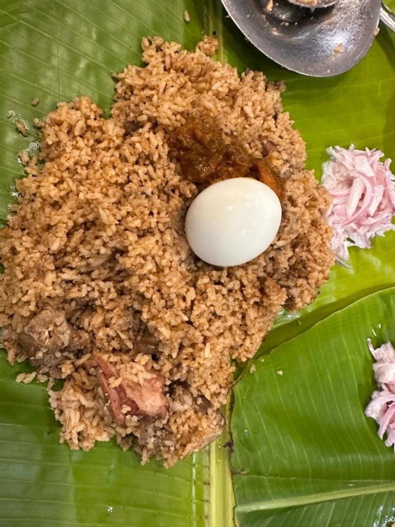 Briyani on a banana leaf with a boiled egg and sliced onions.