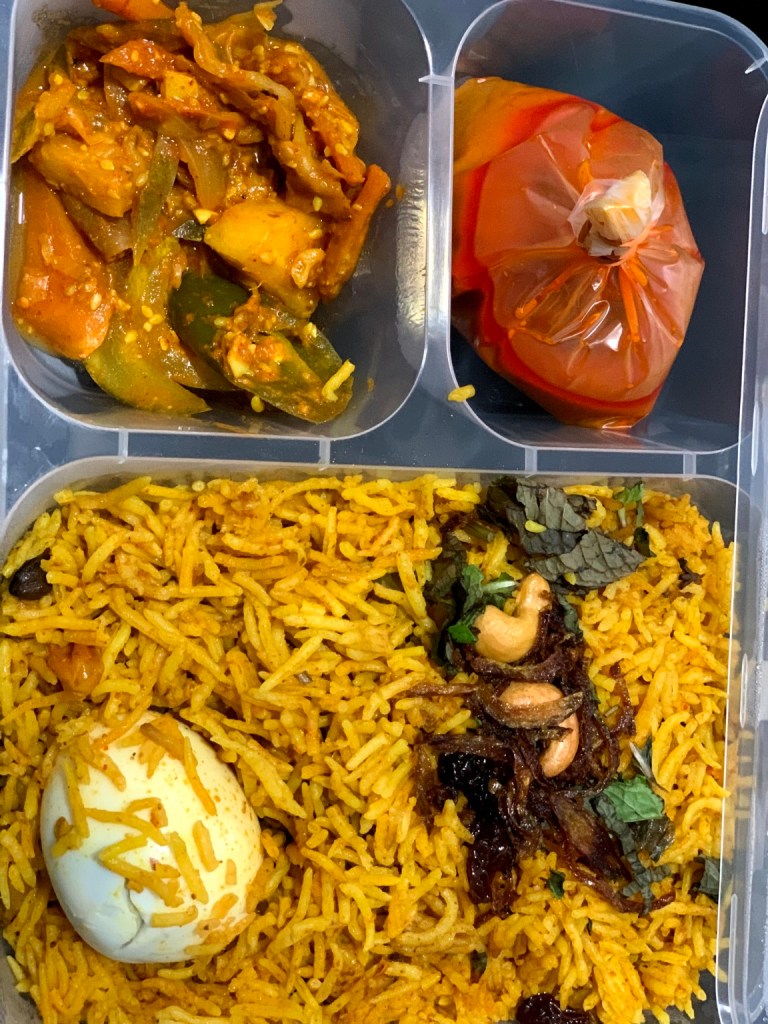 Takeaway briyani topped with a boiled egg, fried onions, cashews and herbs.