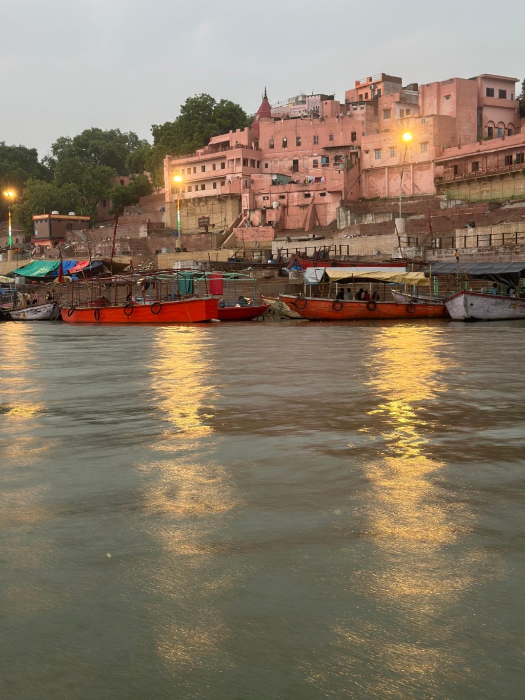 Boats and riverside buildings reflected in the Ganga at dusk.
