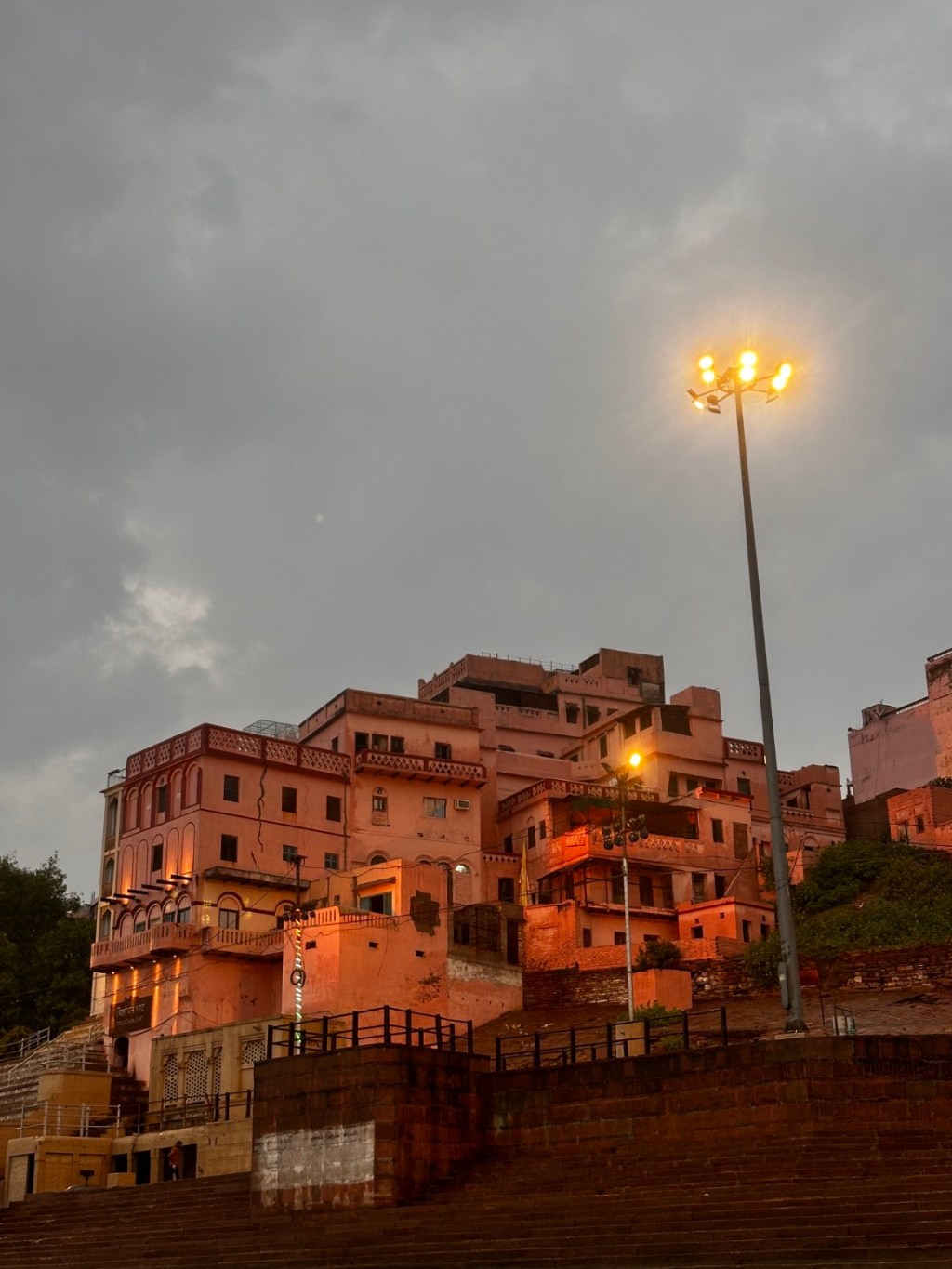 Riverside buildings and lights beneath a grey evening sky in Kashi.