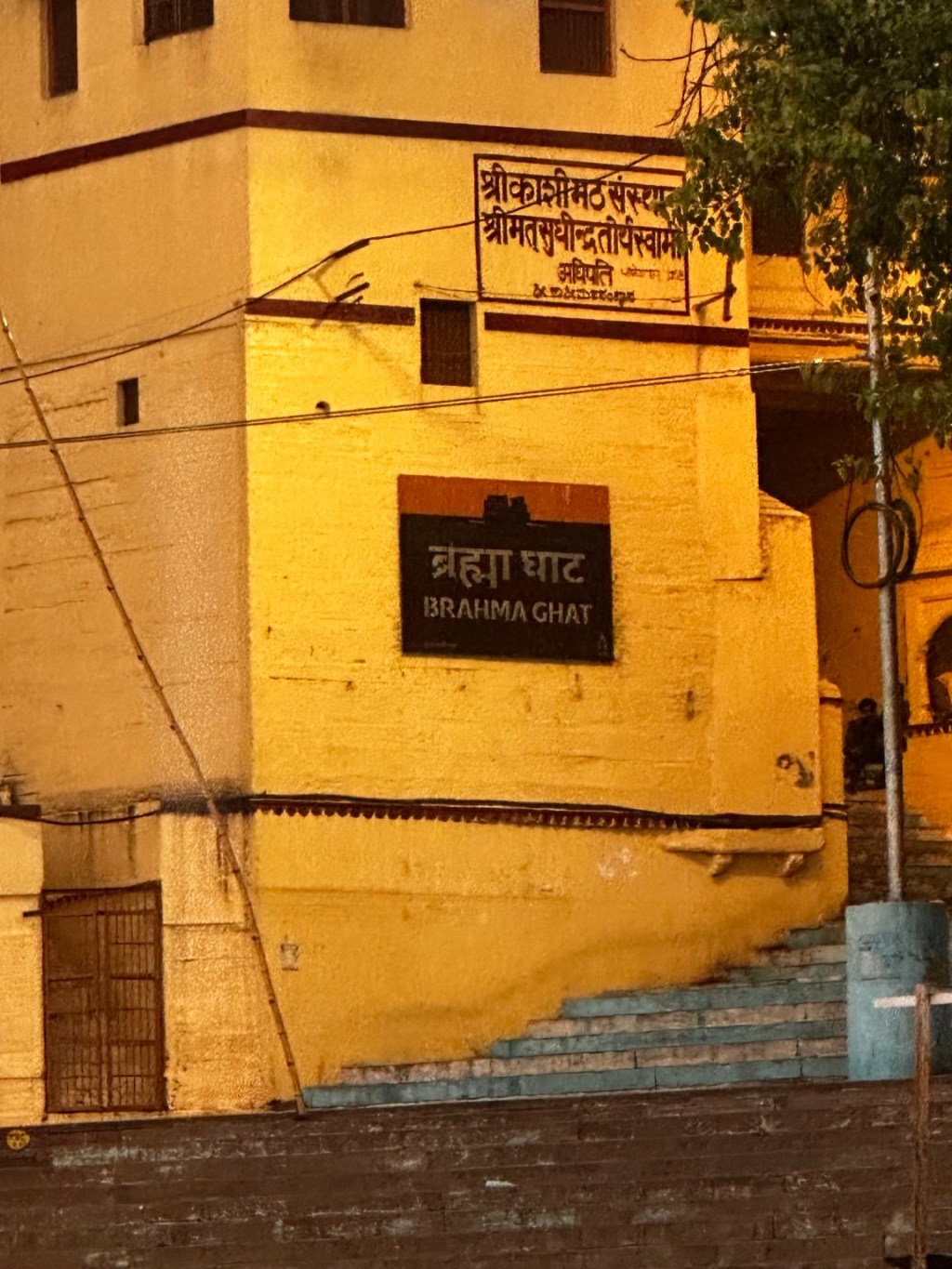 Brahma Ghat sign on a yellow building beside the river.