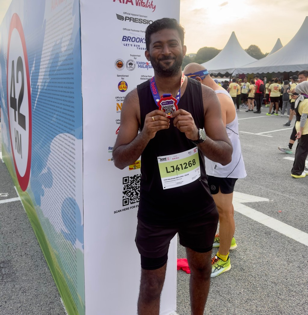 Thana smiling and holding his medal after completing his first half marathon.